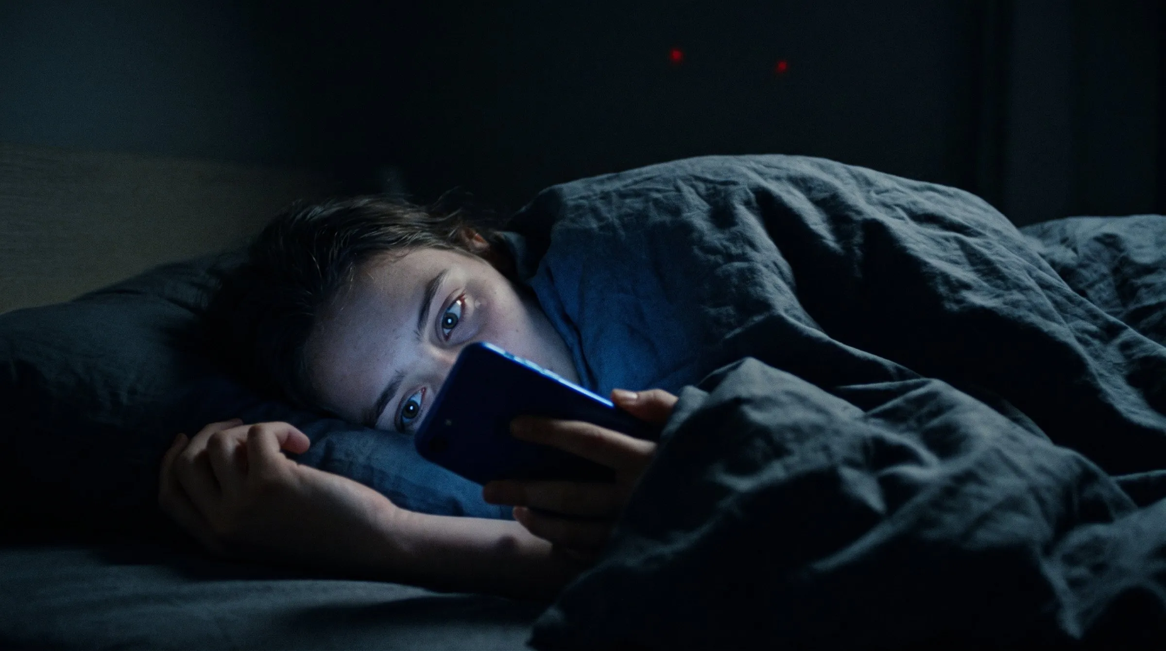 Un’adolescente a letto, al buio, con il viso illuminato dallo schermo del telefono.